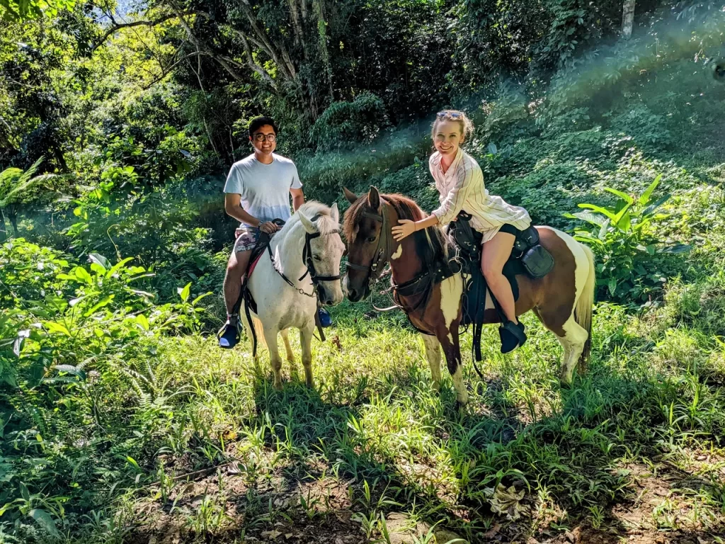 Two people horseback riding with a rainforest backdrop at Rainforest River Ride Adventure in El Yunque National Rainforest, Rio Grande, Puerto Rico